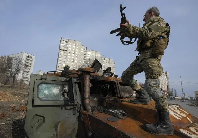 A Ukrainian soldier stands a top a destroyed Russian APC after recent battle in Kharkiv, Ukraine, Saturday, March 26, 2022. (Photo by Efrem Lukatsky/AP Photo)