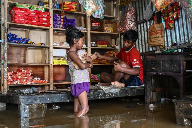 A child buys goods from a partially submerged shop in Companiganj of Sylhet district on June 20, 2024. In Sylhet, lashing rain and rivers swollen by flooding upstream in India also swamped heavily populated areas. (Photo by Munir Uz Zaman/AFP Photo)