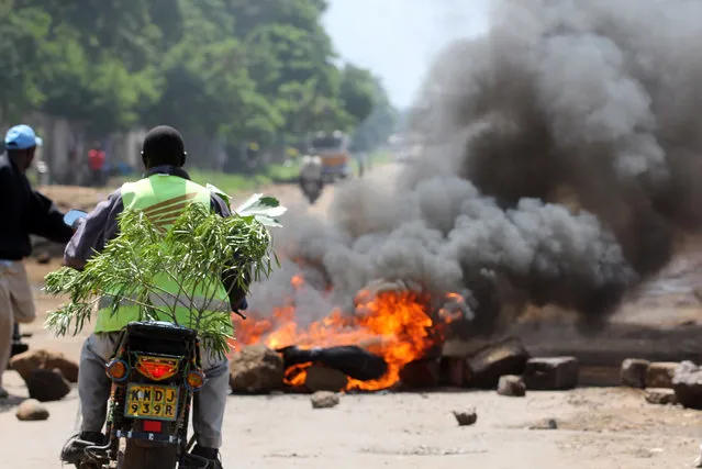 A Kisumu resident stops on his bike to look at burning tyres in the street following protests in Kisumu, Kenya, Monday May 23, 2016. The protests, held for the past four weeks, come before elections next year and are organized by Kenya's main opposition group the Coalitions for Reforms and Democracy. (Photo by James Kayee/AP Photo)
