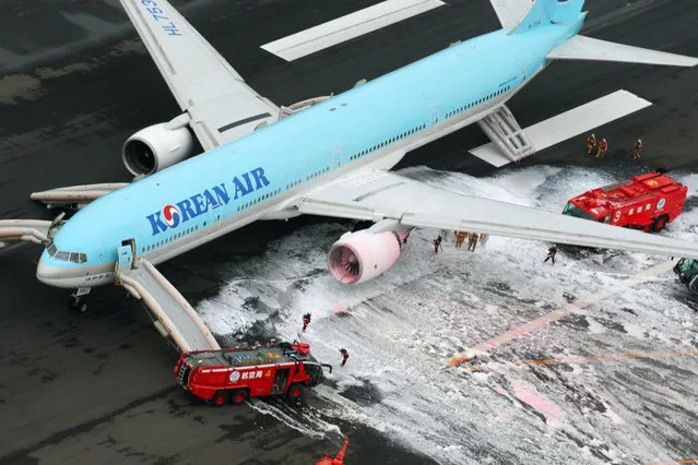 Firefighters gather near an engine of a Korean Air jet following an apparent engine fire on the tarmac at Haneda Airport in Tokyo Friday, May 27, 2016. All the passengers and crew were evacuated unharmed, Japanese media reported. (Photo by Kyodo News via AP Photo)