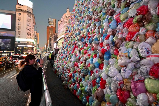 A woman takes pictures of the Obelisk covered with plastic bags as part of an artistic intervention on the eve of World Recycling Day in Buenos Aires on May 16, 2023. (Photo by Luis Robayo/AFP Photo)