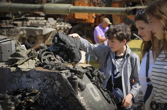 A boy holds a boot of a killed Russian soldier at a destroyed Russian tank installed as a symbol of war in central Kyiv, Ukraine, Tuesday, June 7, 2022. St Michael cathedral is in the background. (Photo by Efrem Lukatsky/AP Photo)