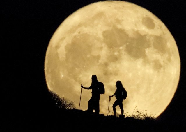 Women walk up a mountain with the full moon known as the “Sturgeon Moon” in the background, in Arguineguin, in the island of Gran Canaria, Spain on August 1, 2023. (Photo by Borja Suarez /Reuters)