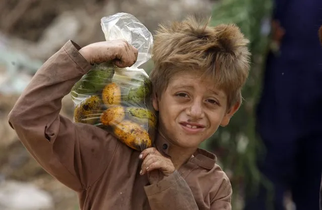 An Afghan refugee boy carries a bag of mangoes on his shoulder in Karachi, Pakistan, Sunday, June 19, 2022. (Photo by Fareed Khan/AP Photo)