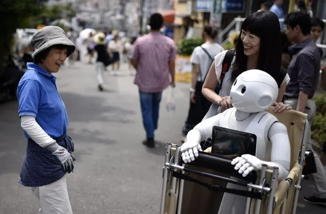 A woman reacts as she sees Tomomi Ota (R) pushing a cart loaded with her humanoid robot Pepper in Tokyo, Japan, 26 June 2016. (Photo by Franck Robichon/EPA)