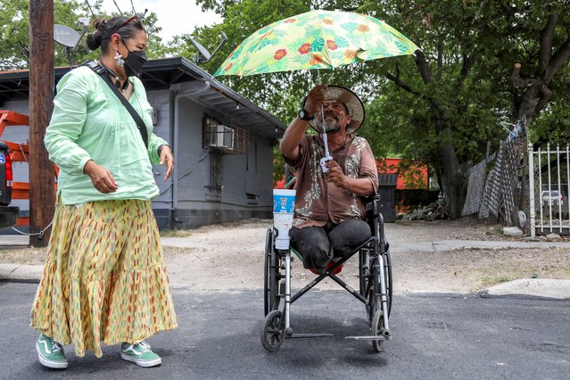 Elpidio Palacios holds an umbrella given to him by Susana Segura, with Bread and Blankets Mutual Aid, to ward off the sun as she gives out water, bananas and hats to unhoused people and others in need during a heat advisory in San Antonio, Texas, U.S., July 21, 2022. (Photo by Lisa Krantz/Reuters)