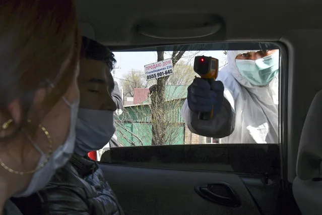 In this Wednesday, March 25, 2020, photo, a medical worker checks temperatures of a car passengers at a checkpoint near Bishkek, Kyrgyzstan. (Photo by Vladimir Voronin/AP Photo)