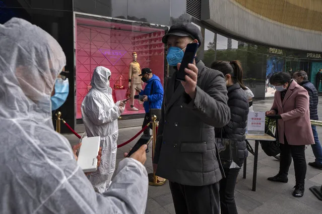In this photo released by Xinhua News Agency, workers wearing protective suits check customers' health QR codes at the entrance of a re-opened shopping mall in in Wuhan in central China's Hubei province, Monday, March 30, 2020. Shopkeepers in the city at the center of China's virus outbreak were reopening Monday but customers were scarce after authorities lifted more of the anti-virus controls that kept tens of millions of people at home for two months. (Photo by Fei Maohua/Xinhua via AP Photo)