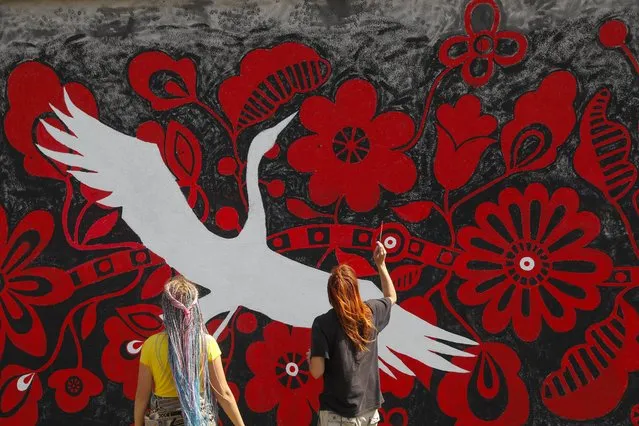 Street artists paint a mural onto a wall near a building in a residential area in Kyiv, Ukraine, 18 August 2022. Ukrainian street artist Yulia Abramova, with friends and colleagues paint a mural depicting a symbolic red the tree of life and white storks as talismans, who symbolically guard Ukraine during the Russian invasion. Russian troops on 24 February entered Ukrainian territory, starting a conflict that has provoked destruction and a humanitarian crisis. (Photo by Sergey Dolzhenko/EPA/EFE)