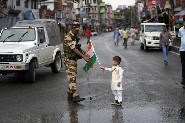 A child, posing for a photograph for his father presents an Indian flag to a security person standing guard outside a venue of Independence Day celebrations in Jammu, India, Monday, Aug.15, 2022. (Photo by Channi Anand/AP Photo)