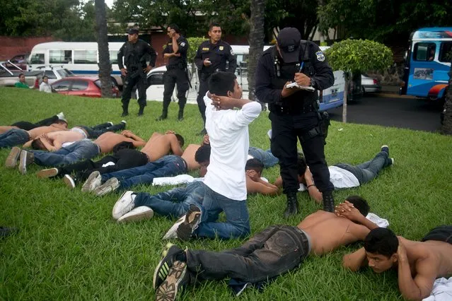 A policeman questions a suspected gang member, whom the police said infiltrated a protest against violence, after he and others were detained in San Salvador, September 5, 2015. The men were detained for being suspicious after they were observed to be communicating gang signs to each other during the protest, according to the police. (Photo by Jessica Orellana/Reuters)
