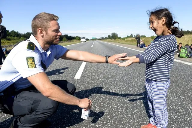 A Danish policeman plays with a migrant girl at the E45 freeway north of Padborg September 9, 2015. Migrants, mainly from Syria and Iraq and hoping to get to Sweden by walking on the freeway, arrived this morning in Padborg on a train from Germany and were placed at a school from where they fled. The police closed the freeway due to security reasons. (Photo by Claus Fisker/Reuters/Scanpix Denmark)