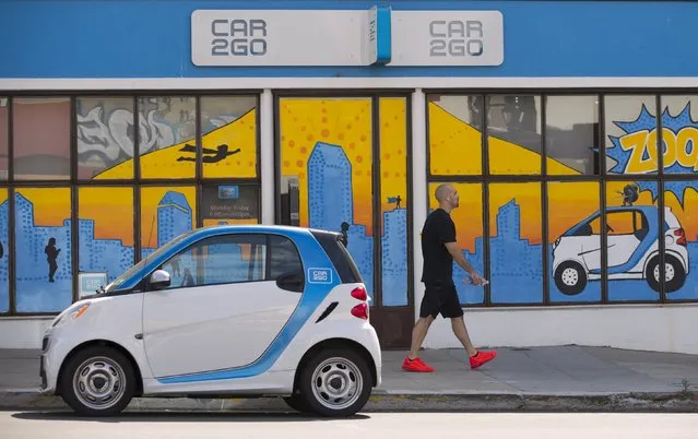 A man walks past an electric car from the car sharing company Car2Go, shown parked in front of their offices in San Diego, California September 1, 2015. (Photo by Mike Blake/Reuters)