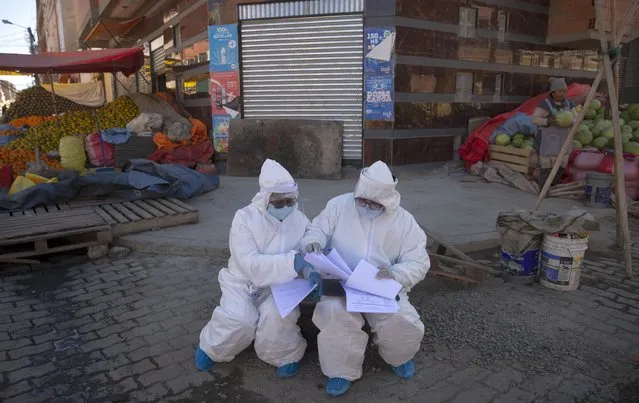 Healthcare workers dressed in full protective gear organize their documents of data they have collected during a house-to-house new coronavirus testing drive, ringed by a produce market in the Villa Dolores neighborhood of El Alto, Bolivia, Saturday, July 18, 2020. (Photo by Juan Karita/AP Photo)