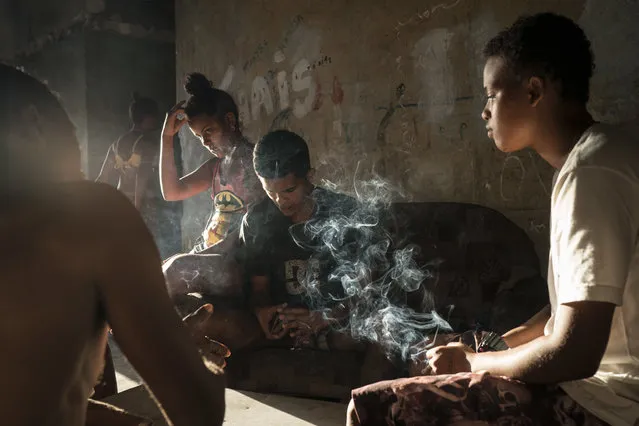 In this September 16, 2017 photo, Jayanne Pessanha, right, smokes a cigarette while playing cards with neighbors in a squatter building that used to house the Brazilian Institute of Geography and Statistics (IBGE) in the Mangueira slum of Rio de Janeiro, Brazil. Pessanha, 20, said her sister died a few years ago after falling from an empty window, and her brother died when he hit his head during a fight. (Photo by Felipe Dana/AP Photo)