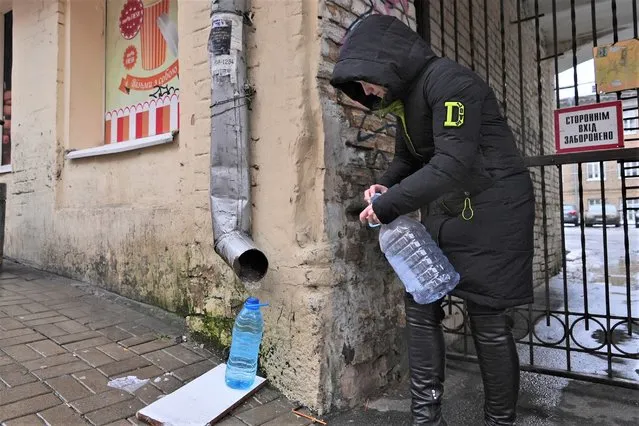 Kateryna Luchkina, a 31-year-old worker at Kyiv’s Department of Health, collects rainwater from a drainpipe in Kyiv, Ukraine, on Thursday. November 24, 2022. Residents of Ukraine's bombed but not cowed capital roamed the streets with empty bottles in search of water and crowded into cafés for warmth, light and power Thursday, switching defiantly into survival mode after new Russian missile strikes the previous day plunged the city of 3 million and much of the country into the dark in winter. (Photo by John Leicester/AP Photo)