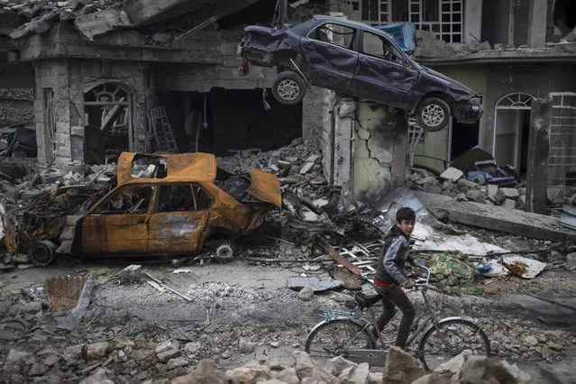 A boy rides his bike past destroyed cars and houses in a neighborhood recently liberated by Iraqi security forces, on the western side of Mosul, Iraq, on March 19, 2017. (Photo by Felipe Dana/AP Photo)