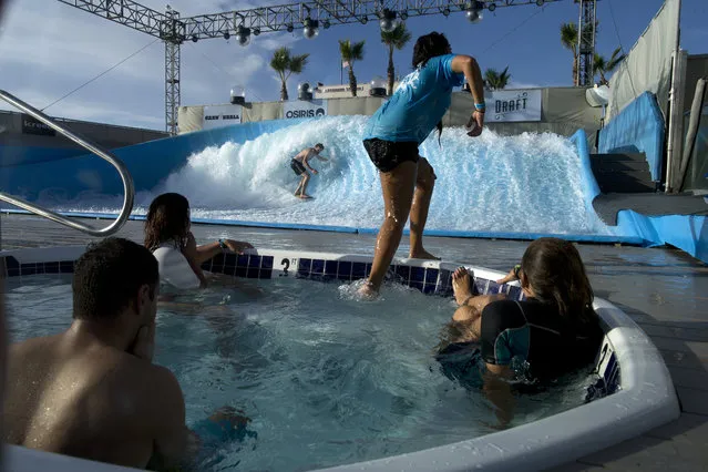 A man rides a wave at the Wavehouse as others stay warm in a Hot tub, Tuesday, October 21, 2014, in San Diego. The machine-generated wave provides surfers on finless boards a chance to hone their skills, just a few feet from a San Diego beach. (Photo by Gregory Bull/AP Photo)