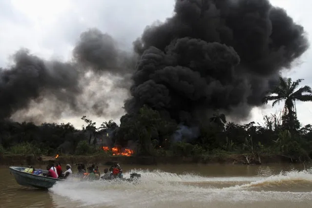 A passenger speedboat churns up the water, while in the background an illegal oil refinery is left burning after a military chase had occurred earlier in a windy creek near river Nun in Nigeria's oil state of Bayelsa December 6, 2012. (Photo by Akintunde Akinleye/Reuters)