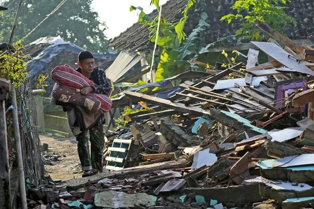A man carries his belongings as he walks through a destroyed neighborhood from Monday's earthquake in Cianjur, West Java, Indonesia, Thursday, November 24, 2022. (Photo by Tatan Syuflana/AP Photo)