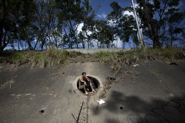 In this December 5, 2017 photo, David Garcia, 19, smokes a cigarette while taking a break during his first week searching the polluted Guaire River for gold and anything valuable he can sell, as he sits on the edge of a drainage pipe, in Caracas, Venezuela. The father of a 4-month-old baby, Garcia said when work dried up organizing block parties he started reselling food he bought after waiting hours in line at grocery stores, but eventually that didn't bring him enough income to feed his family either, so he turned to the river. (Photo by Ariana Cubillos/AP Photo)