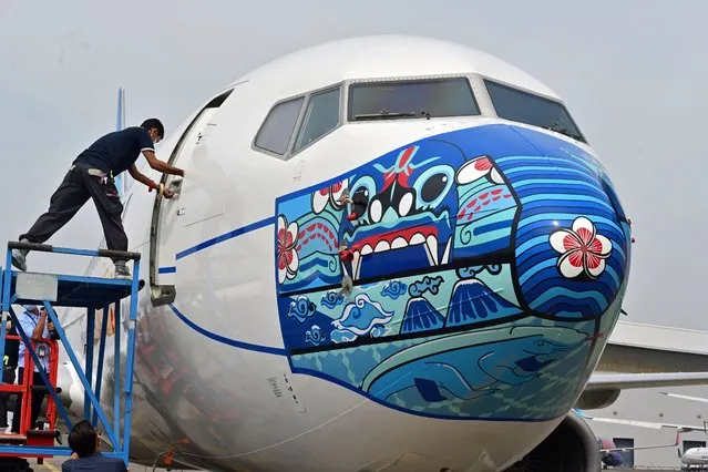 A worker closes a door of a Garuda Indonesia Boeing 373-800 NG with a new face mask design as part of a campaign to promote the wearing of face masks amid the Covid-19 coronavirus, at the airport in Tangerang on October 12, 2020. (Photo by Adek Berry/AFP Photo)