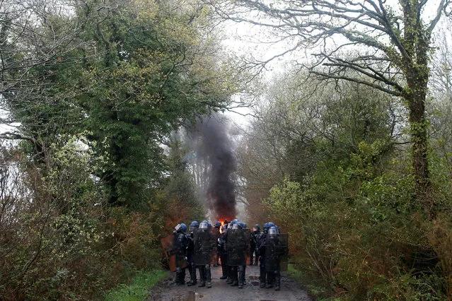 French gendarmes stand on a road near burning debris during an evacuation operation in the zoned ZAD (Deferred Development Zone) in Notre-Dame-des-Landes, near Nantes, France, April 9, 2018. (Photo by Stephane Mahe/Reuters)