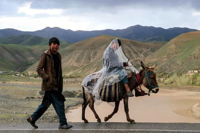 An Afghan boy covers himself with a plastic sheet as he rides on a donkey after rains in Argo district of Badakhshan province on March 20, 2023. (Photo by Omer Abrar/AFP Photo)