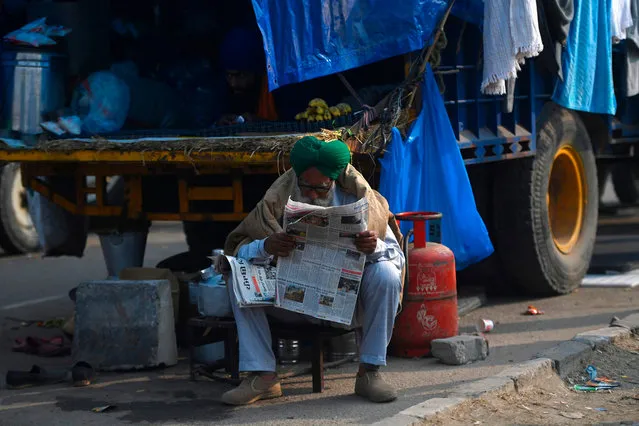 In this picture taken on December 5, 2020 a farmer reads a newspaper next to a vehicle along a blocked a road by police to stop farmers from marching to New Delhi to protest against the central government's recent agricultural reforms, at the Delhi-Haryana state border in Kundli. Behind concertina wire and trucks blockading a major highway into India's capital, thousands of farmers are camping out in the bitter winter cold as they protest against agriculture reforms they fear could destroy their livelihood. (Photo by Money Sharma/AFP Photo)