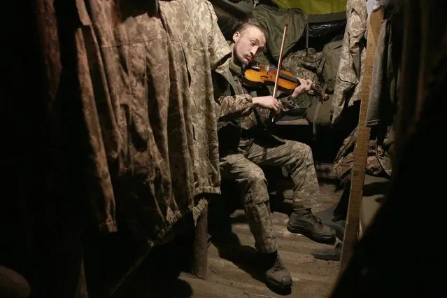 A Ukrainian service man plays the violin in the dugout of a position on the frontline with Russia-backed separatists, not far from Gorlivka, in the Donetsk region, on December 22, 2020. (Photo by Anatolii Stepanov/AFP Photo)