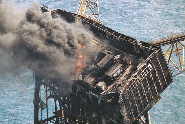 Thick smoke and flames still rise from the mangled remains of the Piper Alpha oil platform in the North Sea off the coast of Scotland in Aberdeen, July, 8, 1988. One-hundred-sixty oil workers were killed when a massive explosion and fire ripped through the platform Wednesday night. (Photo by Dave Caulkin/AP Photo)