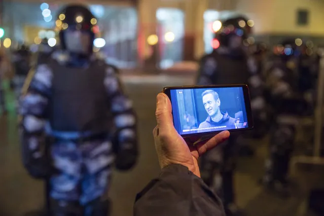 A journalist watches a live stream of a court hearings with the Russian opposition leader Alexei Navalny on a screen as Russian Rosguardia (National Guard) soldiers guard in front of the court in Moscow, Russia, Tuesday, February 2, 2021. A Moscow court has ordered Russian opposition leader Alexei Navalny to prison for more than 2 1/2 years on charges that he violated the terms of his probation while he was recuperating in Germany from nerve-agent poisoning. Navalny, who is the most prominent critic of President Vladimir Putin, had earlier denounced the proceedings as a vain attempt by the Kremlin to scare millions of Russians into submission. (Photo by Pavel Golovkin/AP Photo)