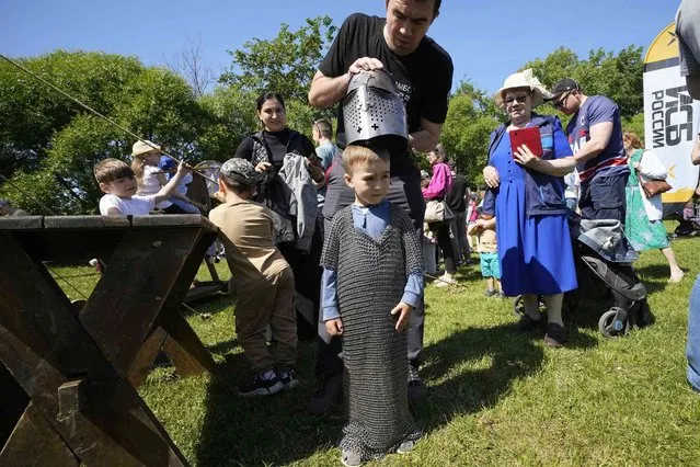 A man tries on a Russian medieval helmet and chain armor to his son during celebrating the Day of Russia at a park in St. Petersburg, Russia, Monday, June 12, 2023. The Day of Russia is celebrated annually on 12 June. (Photo by Dmitri Lovetsky/AP Photo)