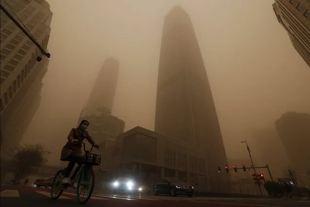 A cyclist and motorists move past office buildings amid a sandstorm during the morning rush hour in the central business district in Beijing, Monday, March 15, 2021. (Photo by Andy Wong/AP Photo)