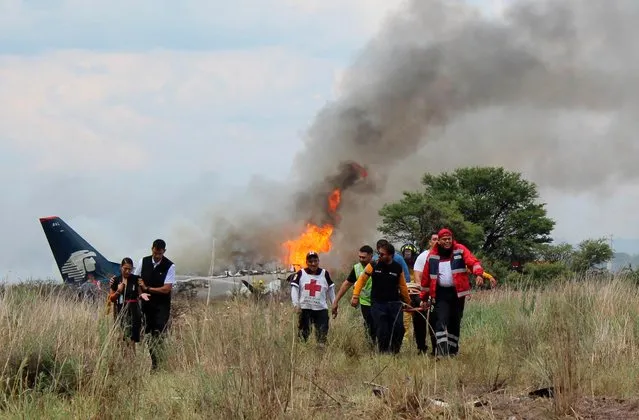 In this photo released by Red Cross Durango communications office, Red Cross workers and rescue workers carry an injured person on a stretcher, right, as airline workers, left, walk away from the site where an Aeromexico airliner crashed in a field near the airport in Durango, Mexico, Tuesday, July 31, 2018. The jetliner crashed while taking off during a severe storm, smacking down in a field nearly intact then catching fire, and officials said it appeared everyone on board escaped the flames. (Photo by Red Cross Durango via AP Photo)