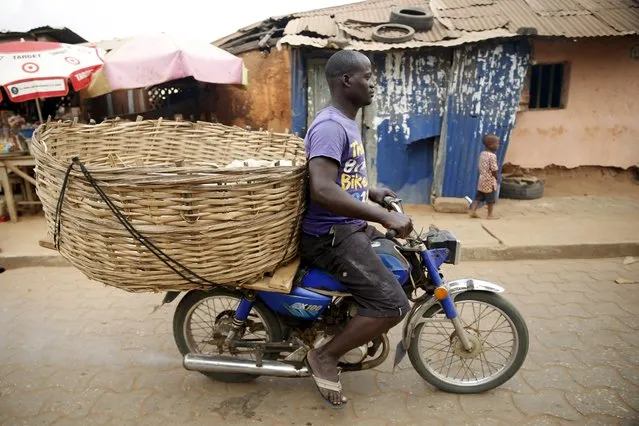 A man rides a motorcycle with a basket at the back through a street in the rustic town of Ouidah January 10, 2016. (Photo by Akintunde Akinleye/Reuters)