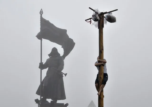 A man tries to climb a wooden pole to get a prize during Maslenitsa celebrations in front of a monument of a revolutionary soldier in Russia's far eastern city of Vladivostok February 22, 2015. Maslenitsa is a pagan holiday marking the end of winter celebrated with pancake eating and shows of strength. (Photo by Yuri Maltsev/Reuters)