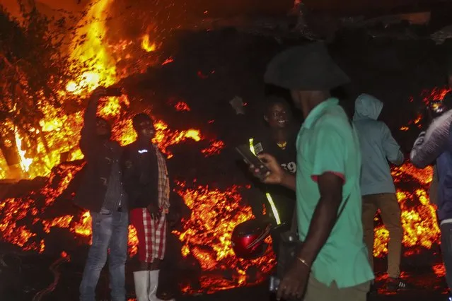 People stand and take selfies in front of lava from the eruption of Mount Nyiragongo, in Buhene, on the outskirts of Goma, Congo in the early hours of Sunday, May 23, 2021. Congo's Mount Nyiragongo erupted for the first time in nearly two decades Saturday, turning the night sky a fiery red and sending lava onto a major highway as panicked residents tried to flee Goma, a city of nearly 2 million. (Photo by Justin Kabumba/AP Photo)