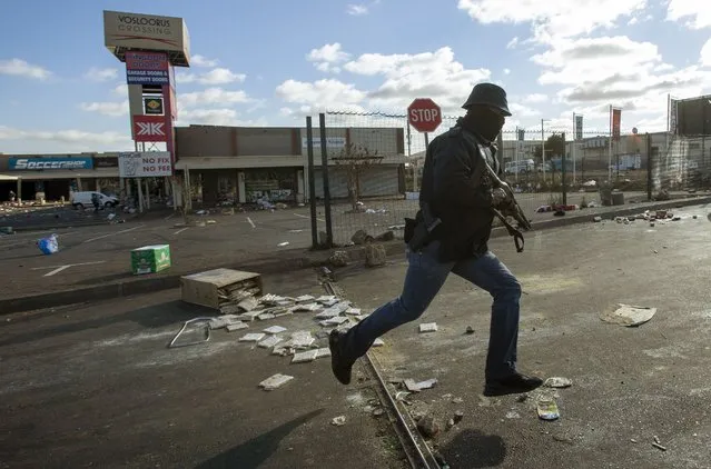 A metro officer dressed in plainclothes, pursues looters looters at a shopping centre in Soweto, Johannesburg, Tuesday July 13, 2021. South Africa's rioting continued Tuesday with the death toll rising to 32 as police and the military struggle to quell the violence in Gauteng and KwaZulu-Natal provinces. The violence started in various parts of KwaZulu-Natal last week when Zuma began serving a 15-month sentence for contempt of court. (Photo by Themba Hadebe/AP Photo)