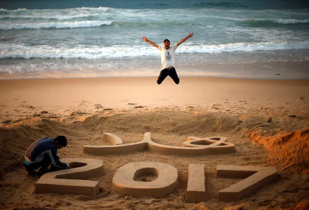 Palestinian artist Yazed Abu Jarad puts the final touches on a sand sculpture that reads “Welcome 2017”, as a man jumps, at a beach in the northern Gaza Strip December 31, 2016. (Photo by Suhaib Salem/Reuters)
