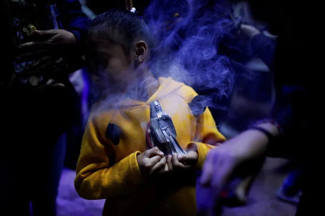 A girl holds a statue of La Santa Muerte (The Saint Death) as a person blows smoke on it during a mass as part of the Day of the Dead celebrations in Nezahualcoyotl, State of Mexico, Mexico on November 2, 2023. (Photo by Raquel Cunha/Reuters)