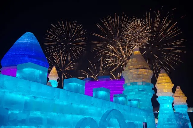 People visit ice sculptures illuminated by coloured lights as fireworks illuminate the night sky marking the opening of the Harbin Ice and Snow Festival to celebrate the new year in Harbin on January 5, 2017. (Photo by Nicolas Asfouri/AFP Photo)