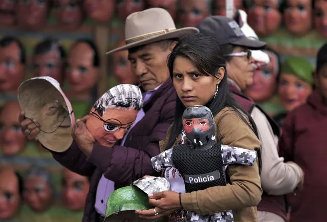 Shoppers carry masks depicting politicians and a papier-mache doll locally known as a “manigote”, purchased at a market in preparation for the New Year's Eve celebrations, in Riobamba, Ecuador, Saturday, Dec. 31, 2022. Come midnight revelers light their manigotes on fire symbolically burning away the bad of the past year in hope that the coming year will be better. (Photo by Juan Diego Montenegro/AP Photo)