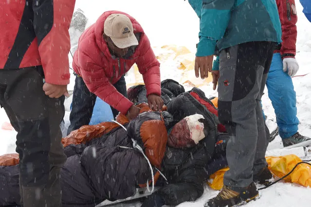 In this photograph taken on April 25, 2015, rescuers tend to a sherpa injured by an avalanche that flattened parts of Everest Base Camp. Rescuers in Nepal are searching frantically for survivors of a huge quake on April 25, that killed nearly 2,000, digging through rubble in the devastated capital Kathmandu and airlifting victims of an avalanche at Everest base camp. (Photo by Roberto Schmidt/AFP Photo)