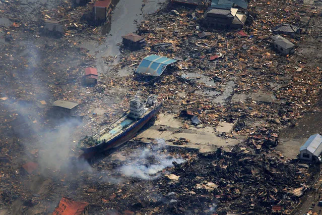 In this March 13, 2011 file aerial photo, a ship washed away by tsunami sits amid debris in Kesennuma, Miyagi Prefecture, northeastern Japan, two days after a powerful earthquake and tsunami hit the area. (Photo by Itsuo Inouye/AP Photo)