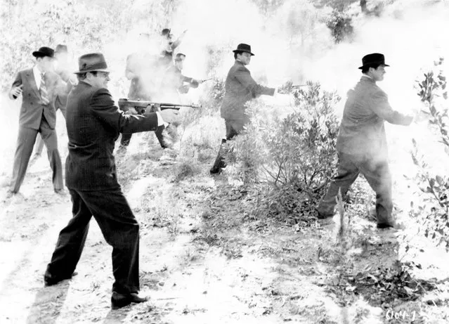 A group of men in suits and hats are obscured by the smoke from the guns, including Thompson submachine guns, shotguns, and revolvers, that they are firing in a shrubland, USA, 1930s. (Photo by Vintage Images/Getty Images)