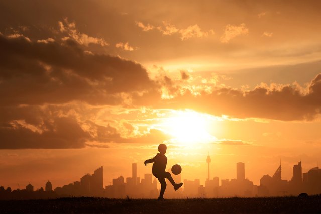 A boy kicks a football in Dudley Page Reserve as storm clouds gather over the city skyline on September 30, 2021 in Sydney, Australia. The Bureau of Meteorology has issued severe storm warnings for the city. (Photo by Mark Evans/Getty Images)