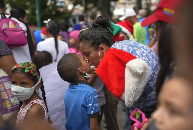 A mother kisses her son as they parade with other mothers and children from soup kitchen, celebrating Christmas in the Mamera neighborhood of Caracas, Venezuela, Thursday, December 16, 2021. (Photo by Ariana Cubillos/AP Photo)