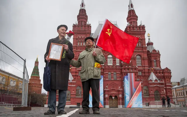 Two Russian communists' supporters stand in Red Square holding a portrait of Vladimir Lenin and a red flag as they wait to visit the Mausoleum of the Soviet founder Vladimir Lenin to mark the 146th anniversary of his birth in Moscow, Russia, Friday, April 22, 2016. (Photo by Pavel Golovkin/AP Photo)