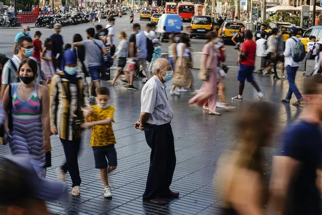 A man wearing a a face mask to protect against the spread of coronavirus pauses as people walk along a street in downtown Barcelona, Spain, July 3, 2021. With one of Europe's highest vaccination rates and its most pandemic-battered economies, the Spanish government is laying the groundwork to approach the virus in much the same way countries deal with flu or measles. (Photo by Joan Mateu/AP Photo/File)
